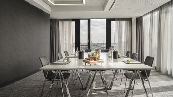 Boardroom im ATLANTIC Hotel Münster Moderner Konferenzraum im ATLANTIC Hotel Münster mit großem Tisch, Stühlen, Wasserflaschen und Obst, helle Fensterfront.