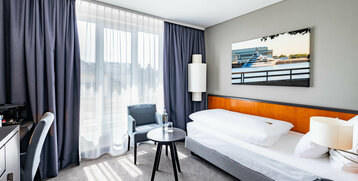 Helles Hotelzimmer mit Einzelbett, Schreibtisch, Sessel, rundem Tisch und großem Fenster im ATLANTIC Hotel Vegesack.