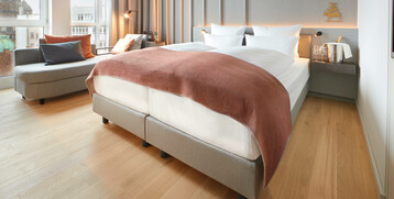 Modernes Hotelzimmer mit Doppelbett, gemütlicher Sitzecke, Holzfußboden und Blick auf Bremer Gebäude.