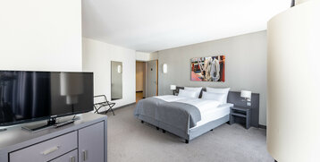 Helles Hotelzimmer mit Doppelbett, TV, Spiegel und maritimem Wandbild im ATLANTIC Hotel Vegesack, Bremen.