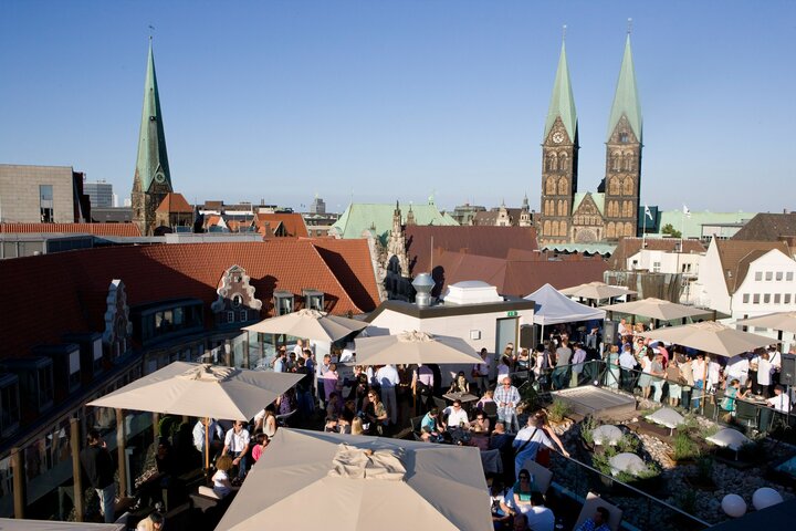 THE GRAND TERRACE with the unique panoramic view Roof terrace of the ATLANTIC Grand Hotel Bremen with guests, sunshades and a view of Bremen's historic church towers.
