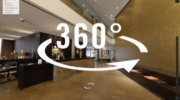 Moderne Hotellobby mit Rezeption, Sitzbereich und goldener Wand; 360-Grad-Ansicht verfügbar.