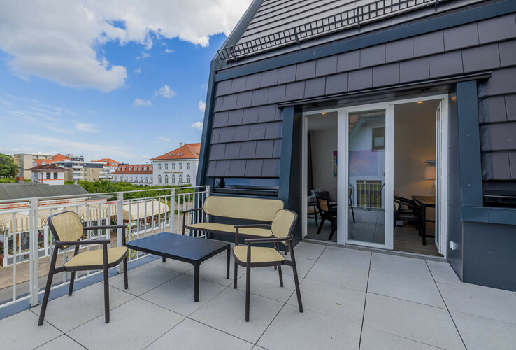 Dachterrasse mit Sitzmöbeln und Blick auf historische Gebäude des ATLANTIC Grand Hotel Travemünde im Hintergrund.