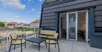 Roof terrace with seating and a view of the historic buildings of the ATLANTIC Grand Hotel Travemünde in the background.