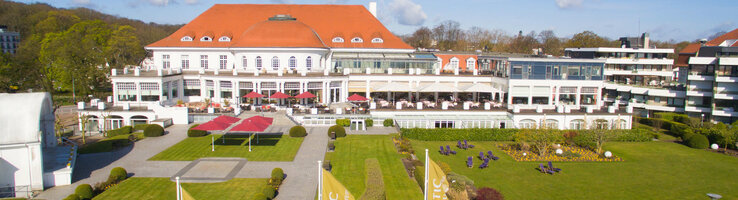 ATLANTIC Grand Hotel Travemünde ATLANTIC Grand Hotel Travemünde: Historisches Gebäude mit rotem Dach, gepflegter Garten, gelbe Fahnen im Vordergrund.