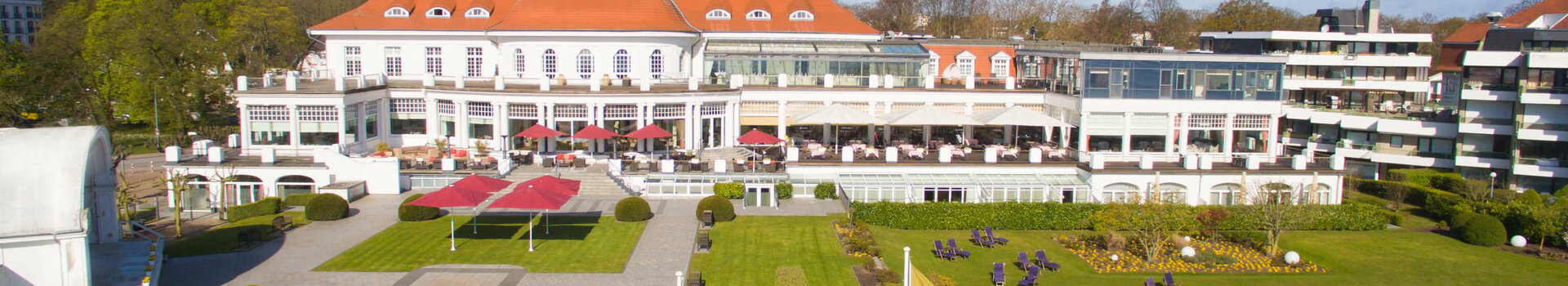 ATLANTIC Grand Hotel Travemünde ATLANTIC Grand Hotel Travemünde: Historisches Gebäude mit rotem Dach, gepflegter Garten, gelbe Fahnen im Vordergrund.