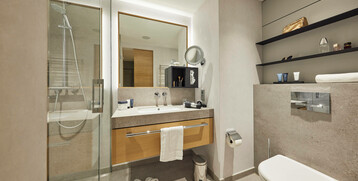 Modernes Hotelbadezimmer mit Dusche, Waschbecken, Spiegel, WC und Regalen mit Pflegeprodukten im ATLANTIC Hotel Heidelberg.