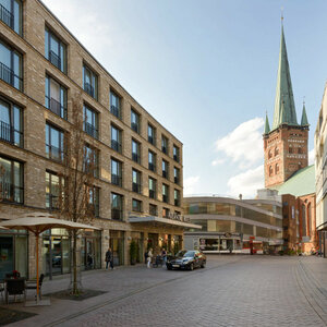 Street view of the ATLANTIC Hotel Lübeck with brick facade, next to it a church with a high tower.