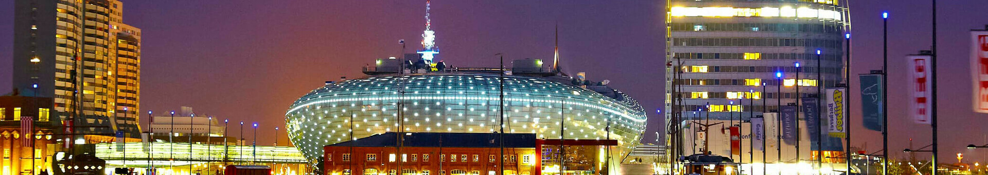 Illuminated skyline of Bremerhaven at night with modern buildings and reflecting water in the foreground.