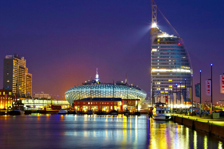 Illuminated skyline of Bremerhaven at night with modern buildings and reflecting water in the foreground.