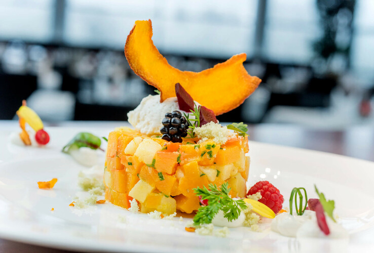 Elegantes Dessert mit frischen Früchten, Beeren und Kräutern, kunstvoll auf einem weißen Teller angerichtet.