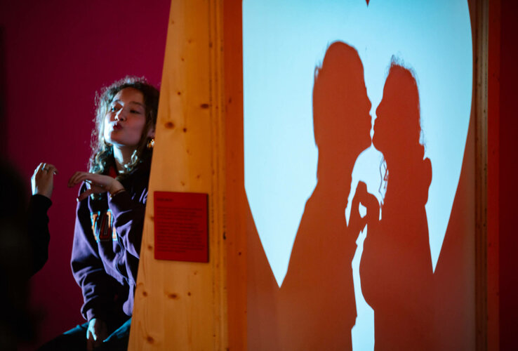 Frau vor rotem Hintergrund, wirft Schatten eines Paares, das sich küsst, auf eine herzförmige Leinwand.