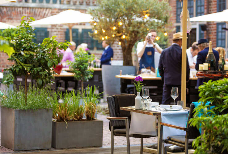 Cozy hotel garden with covered tables, plants and guests under parasols.