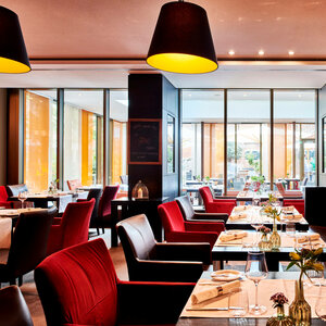 Modernes Restaurant im ATLANTIC Grand Hotel Bremen mit eleganten roten Stühlen, gedeckten Tischen und großen Fenstern.