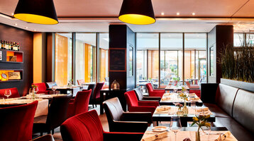 Modern restaurant in the ATLANTIC Grand Hotel Bremen with elegant red chairs, laid tables and large windows.