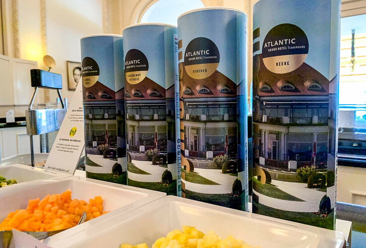 Müsli-Station im ATLANTIC Grand Hotel Travemünde mit verschiedenen Müslidosen und frischen Obststücken.