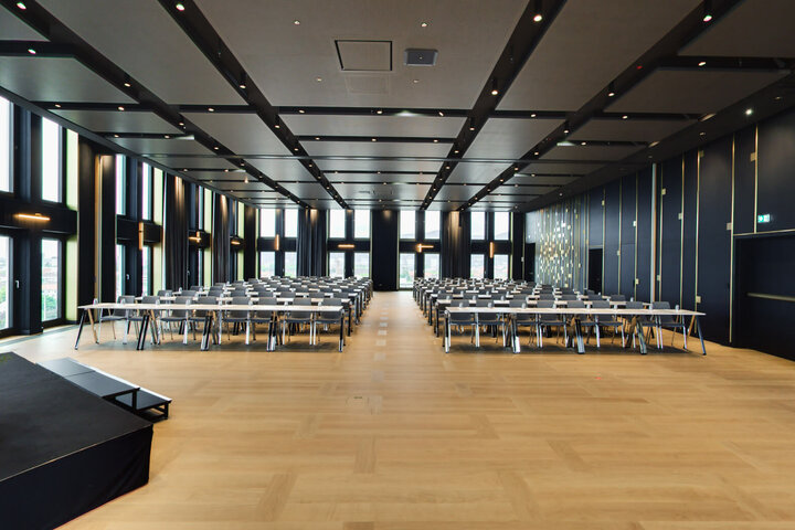 Moderner, großer Konferenzraum im ATLANTIC Hotel Heidelberg mit Reihen von Tischen und Stühlen, Bühne links, elegante Dekoration.