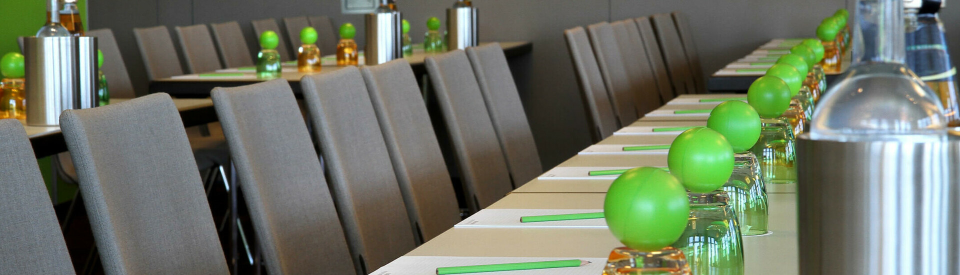 Konferenzraum mit grauen Stühlen, Tischen, grünen Dekobällen und Wasserflaschen im ATLANTIC Hotel Kiel.