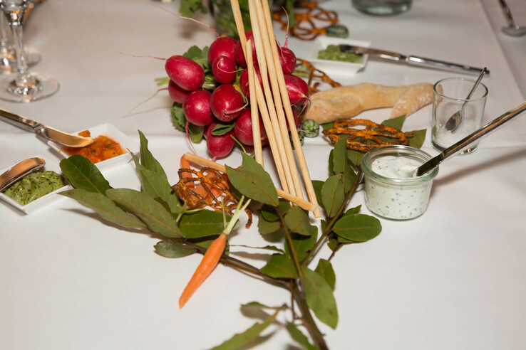 A table laid with radishes, breadsticks, dips and herbs on a white tablecloth.