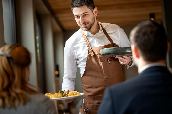 Moderne Restaurants im ATLANTIC Hotel Landgut Horn Bremen  Kellner im ATLANTIC Hotel Landgut Horn serviert lächelnd Speisen an Gäste in elegantem Restaurantambiente.
