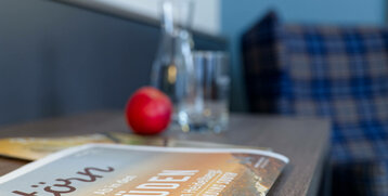 Ein Tisch mit einem Magazin, einem roten Apfel, einem Glas und einer Karaffe im ATLANTIC Hotel Landgut Horn Bremen.