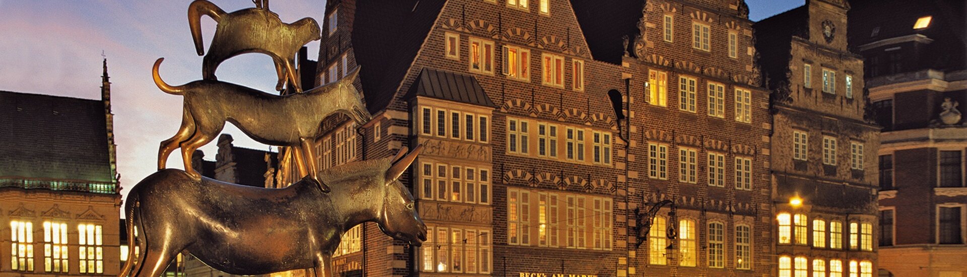 Statue of the Bremen Town Musicians in front of historic buildings in the evening light.