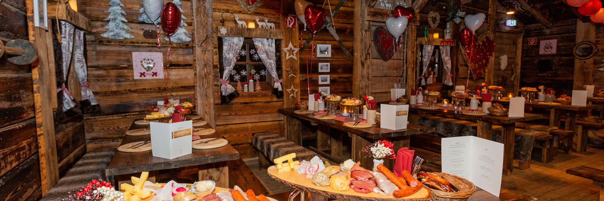 Gemütliche Holzhütte mit festlich gedeckten Tischen, roter Dekoration und rustikalen Speisenplatten.