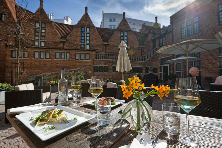 Terrasse des ATLANTIC Grand Hotel Bremen mit gedecktem Tisch, Speisen, Blumen und historischem Backsteingebäude im Hintergrund.