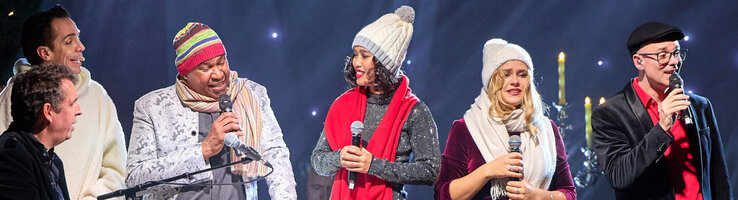 Eine Gruppe von Menschen singt auf einer Bühne mit festlicher Beleuchtung und Dekoration.