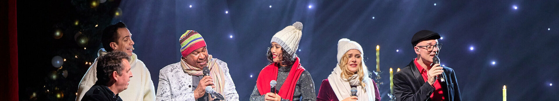 ATLANTIC Hotel Münster Firmenweihnachtsfeier im Engelsaal A group of people sing on a stage with festive lighting and decorations.