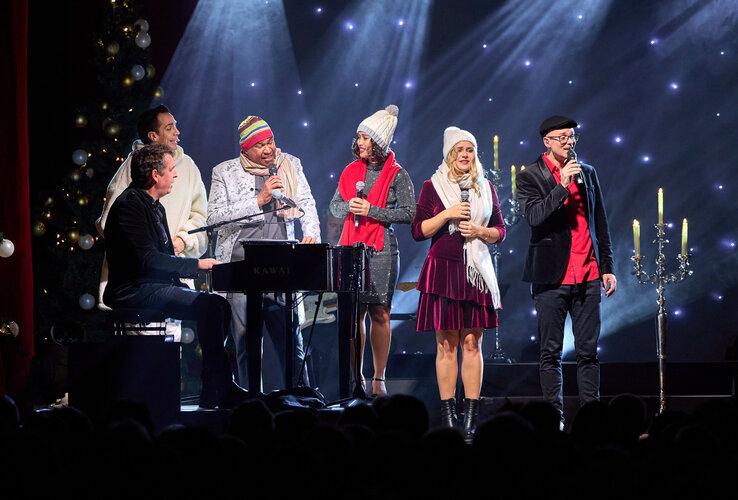 Eine Gruppe von Menschen singt auf einer Bühne mit festlicher Beleuchtung und Dekoration.