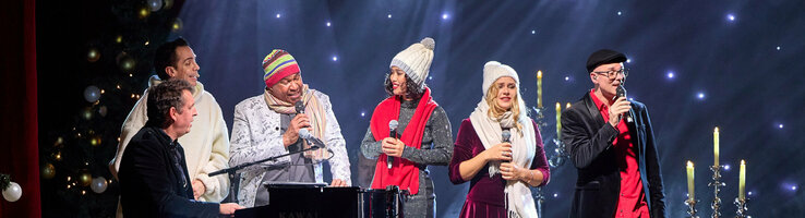 ATLANTIC Hotel Münster Firmenweihnachtsfeier im Engelsaal A group of people sing on a stage with festive lighting and decorations.