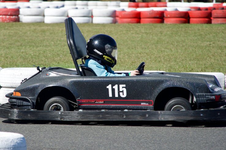 Kind fährt Go-Kart auf Rennstrecke mit Reifenbarrieren im Hintergrund.
