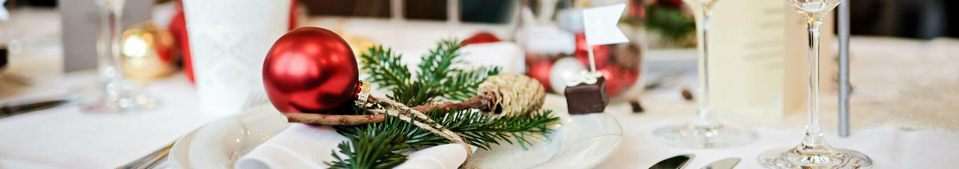 Festlich gedeckter Tisch mit roter Kugel, Tannenzweig und Weingläsern im ATLANTIC Hotel Wilhelmshaven.
