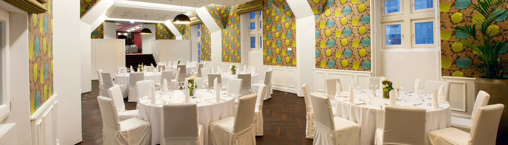 Runde Tische im Scotland Saal des ATLANTIC Grand Hotels Bremen Eleganter Bankettsaal im ATLANTIC Grand Hotel Bremen mit runden, weiß gedeckten Tischen und bunter Tapete.