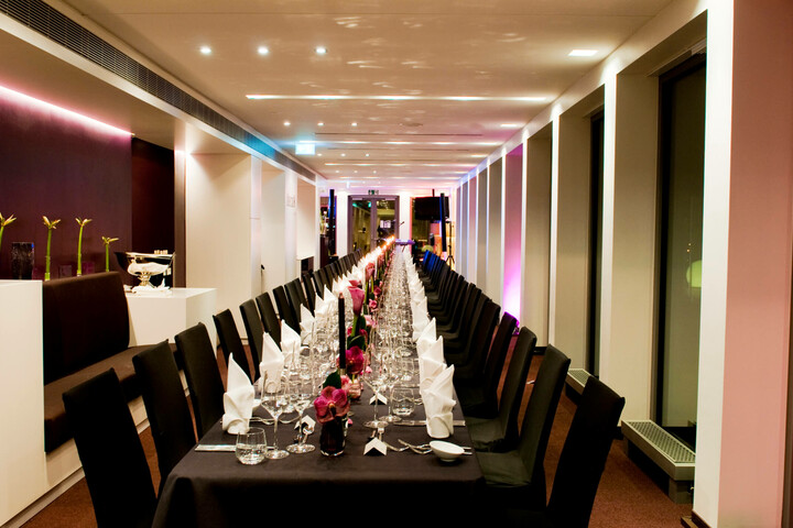 Festliche Tafel auf DECK 8 – die Bar Eleganter, festlich gedeckter langer Tisch in modernem Raum mit gedämpfter Beleuchtung im ATLANTIC Hotel Kiel.