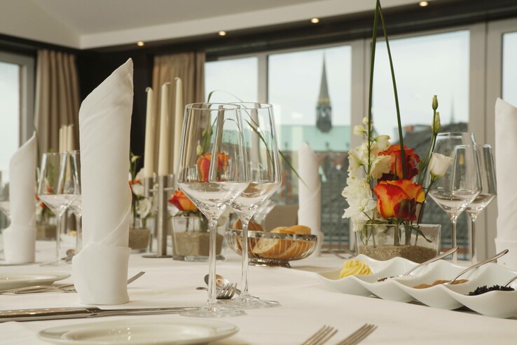 Elegant table setting with floral decorations and wine glasses at the ATLANTIC Hotel Lübeck. Background: View of the city.