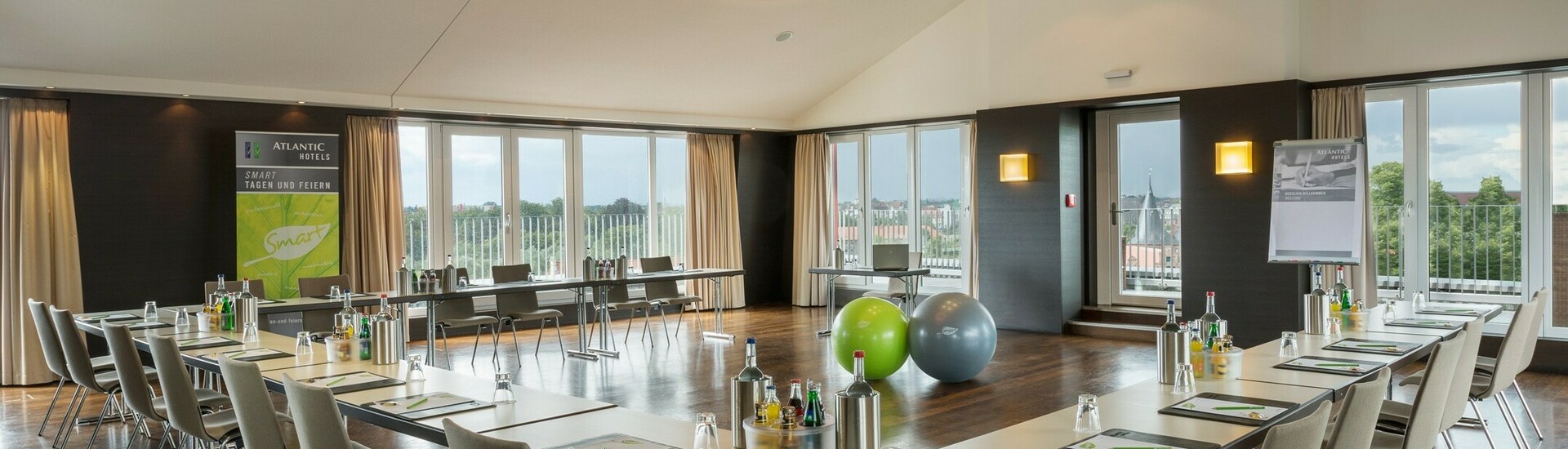Heller Konferenzraum mit U-förmiger Tischanordnung, modernem Design und Blick auf Lübeck durch große Fenster.