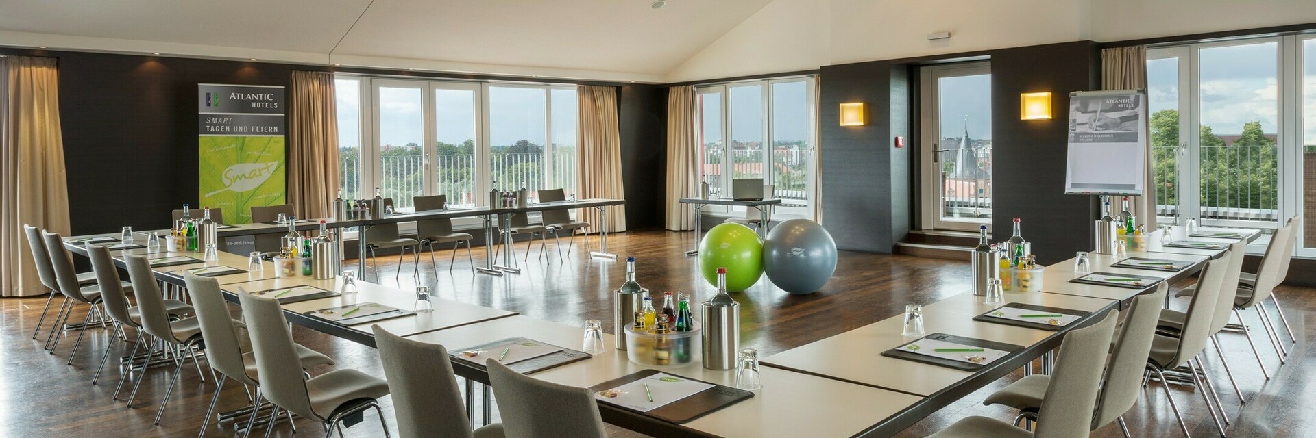 Bright conference room with U-shaped table arrangement, modern design and view of Lübeck through large windows.