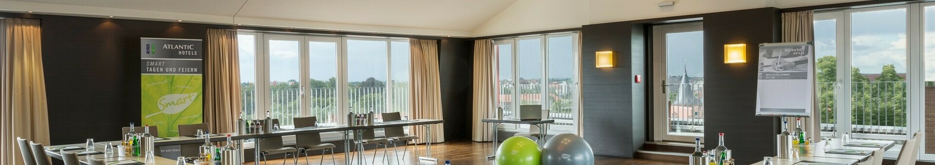 Bright conference room with U-shaped table arrangement, modern design and view of Lübeck through large windows.