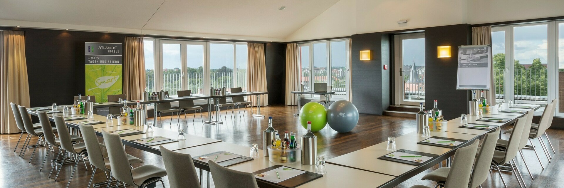 Heller Konferenzraum mit U-förmiger Tischanordnung, modernem Design und Blick auf Lübeck durch große Fenster.