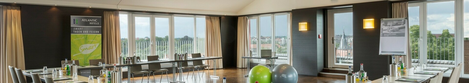 Heller Konferenzraum mit U-förmiger Tischanordnung, modernem Design und Blick auf Lübeck durch große Fenster.