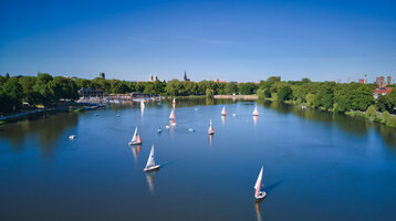 Naherholungsgebiet Aasee in Münster Segelboote auf dem Aasee in Münster, umgeben von grünen Bäumen und blauem Himmel.