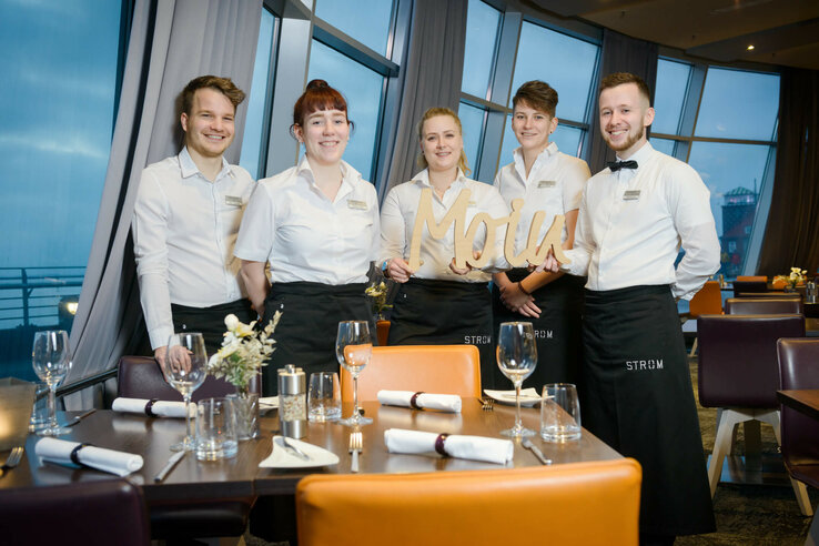 Das Restaurantteam des ATLANTIC Hotel Sail City steht lächelnd am gedeckten Tisch.