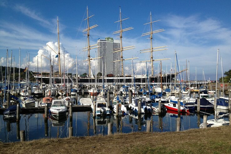 Yachthafen mit Segelbooten vor dem ATLANTIC Grand Hotel Travemünde und einem großen Segelschiff im Hintergrund.