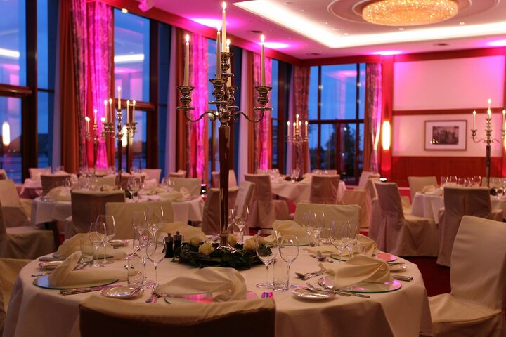 Eleganter Bankettsaal mit runden, weiß gedeckten Tischen, Kerzenleuchtern und rosa Beleuchtung.