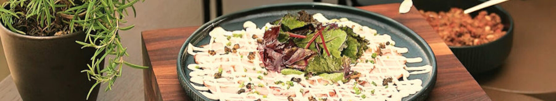 Verschiedene Salate und Dips auf Holzständern, umgeben von frischen Kräutern in Töpfen.