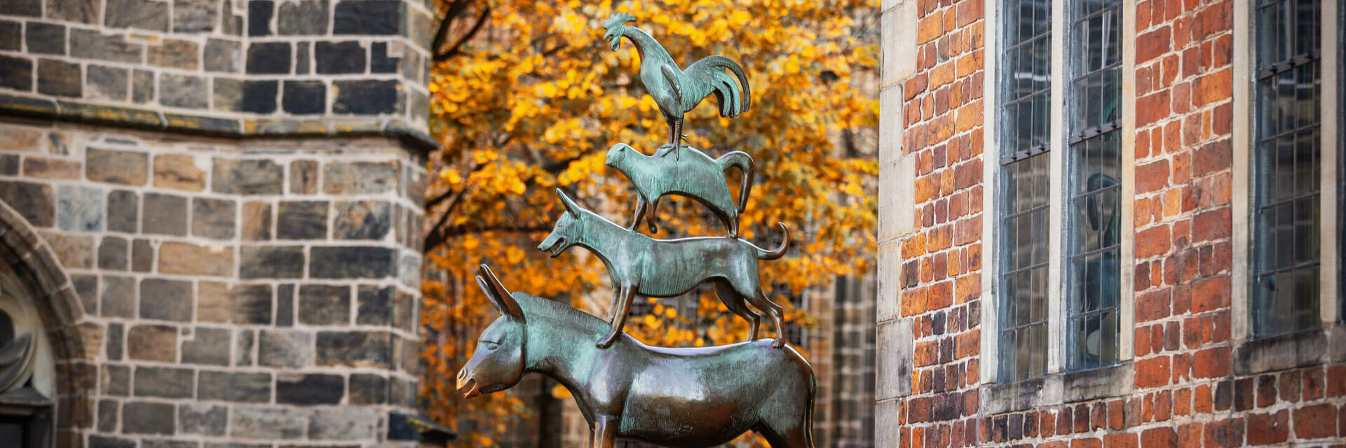 Bronze statue of the Bremen Town Musicians in front of an autumnal tree and brick building.