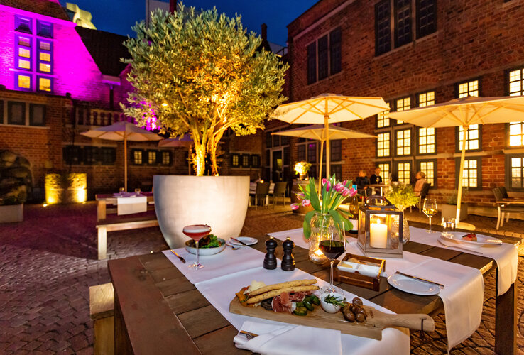 Illuminated hotel terrace with laid tables, candles, flowers and food at the ATLANTIC Grand Hotel Bremen.