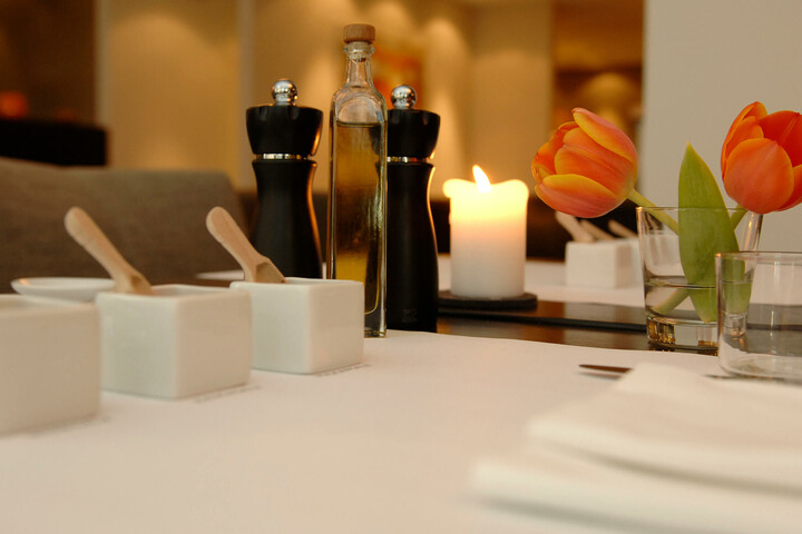Eleganter, gedeckter Tisch mit Kerze, Tulpen, Ölflasche und Gewürzmühlen im ATLANTIC Hotel Lübeck.